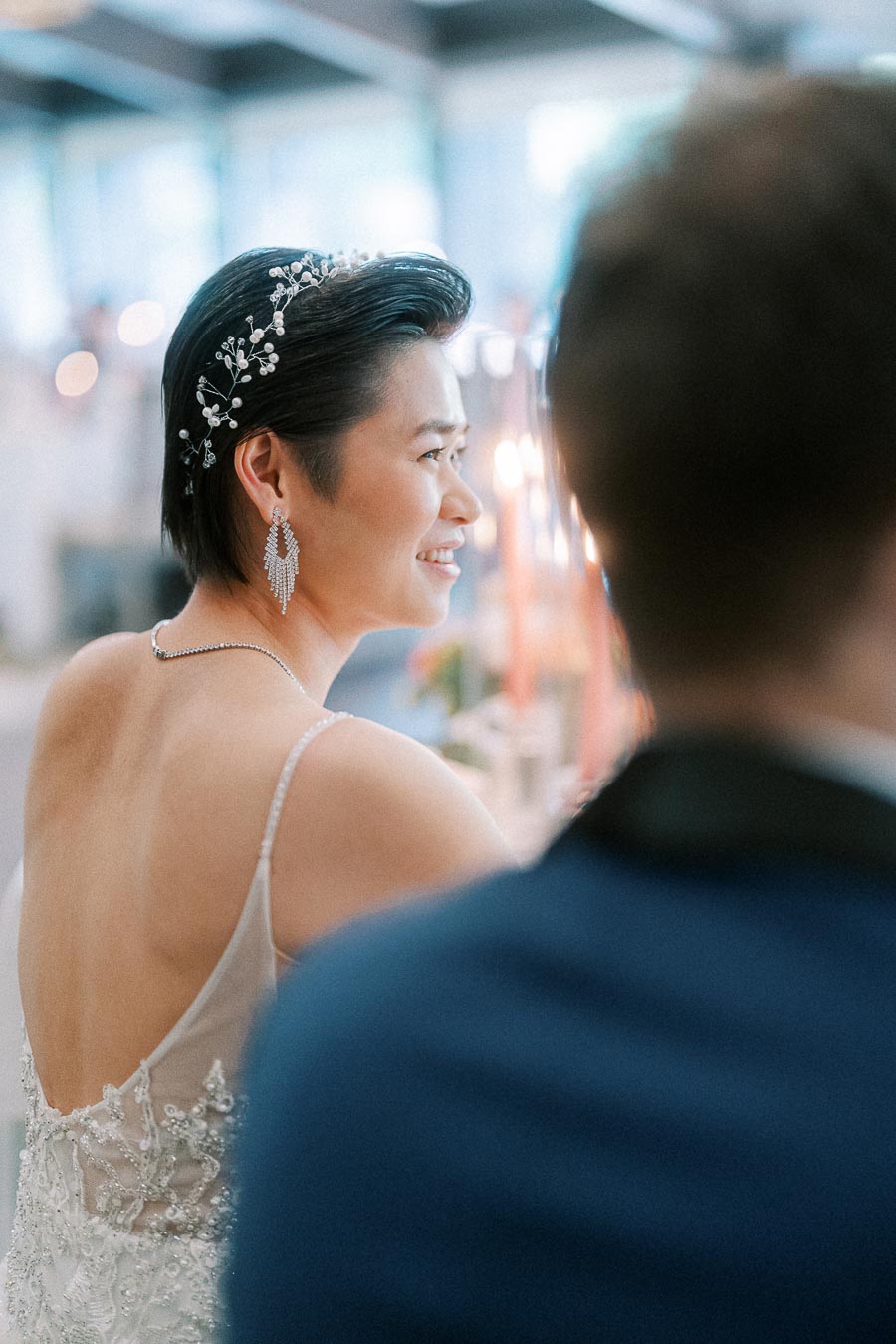 Miffy smiles over her shoulder in a beaded wedding dress and pearl hairpiece, with Rawle blurred in the foreground.