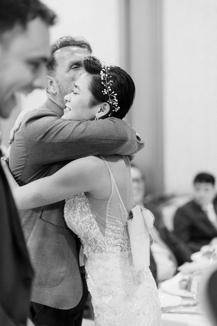 Miffy in a beaded wedding dress and pearl hairpiece hugs a smiling guest during the reception.