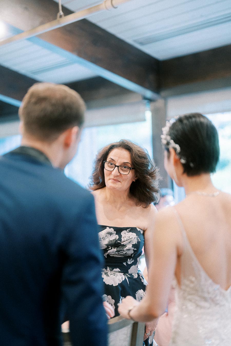 Bride and groom listen to a woman speaking during their indoor wedding ceremony at Ancaster Mill.