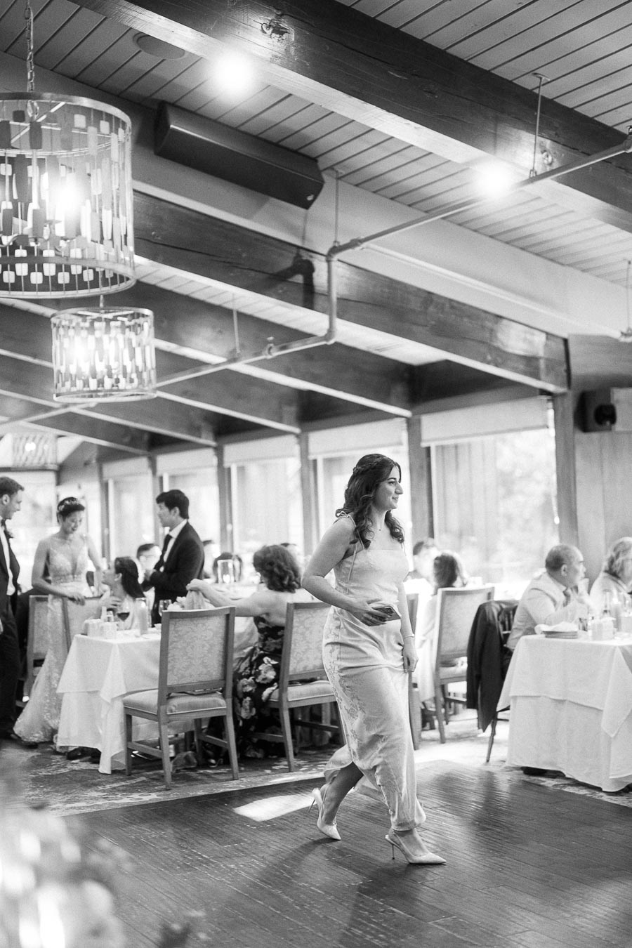 Woman in a satin dress walking across the reception dance floor as guests sit at round tables.