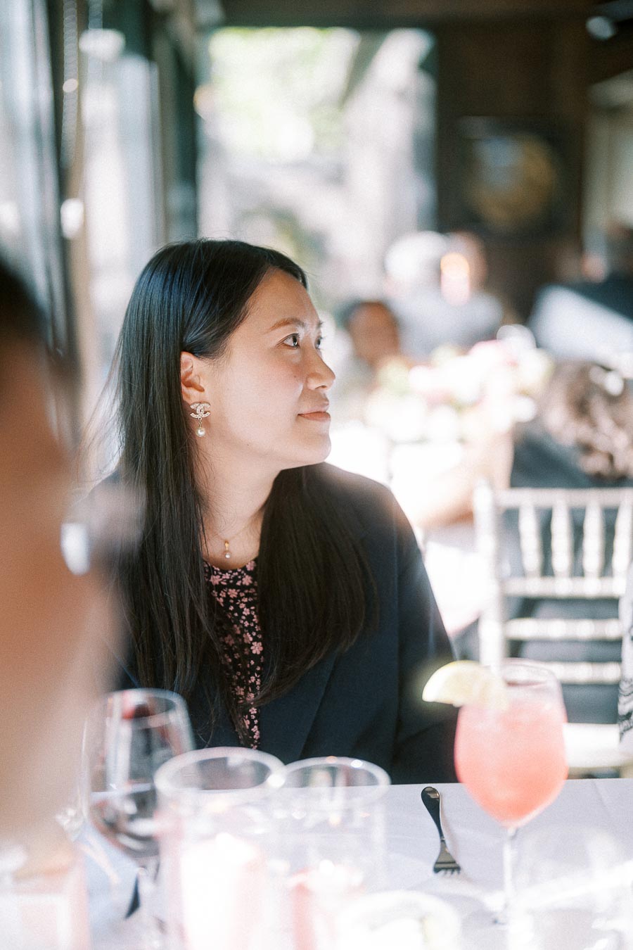 Woman in a dark blazer seated at a wedding reception table with drinks and soft window light