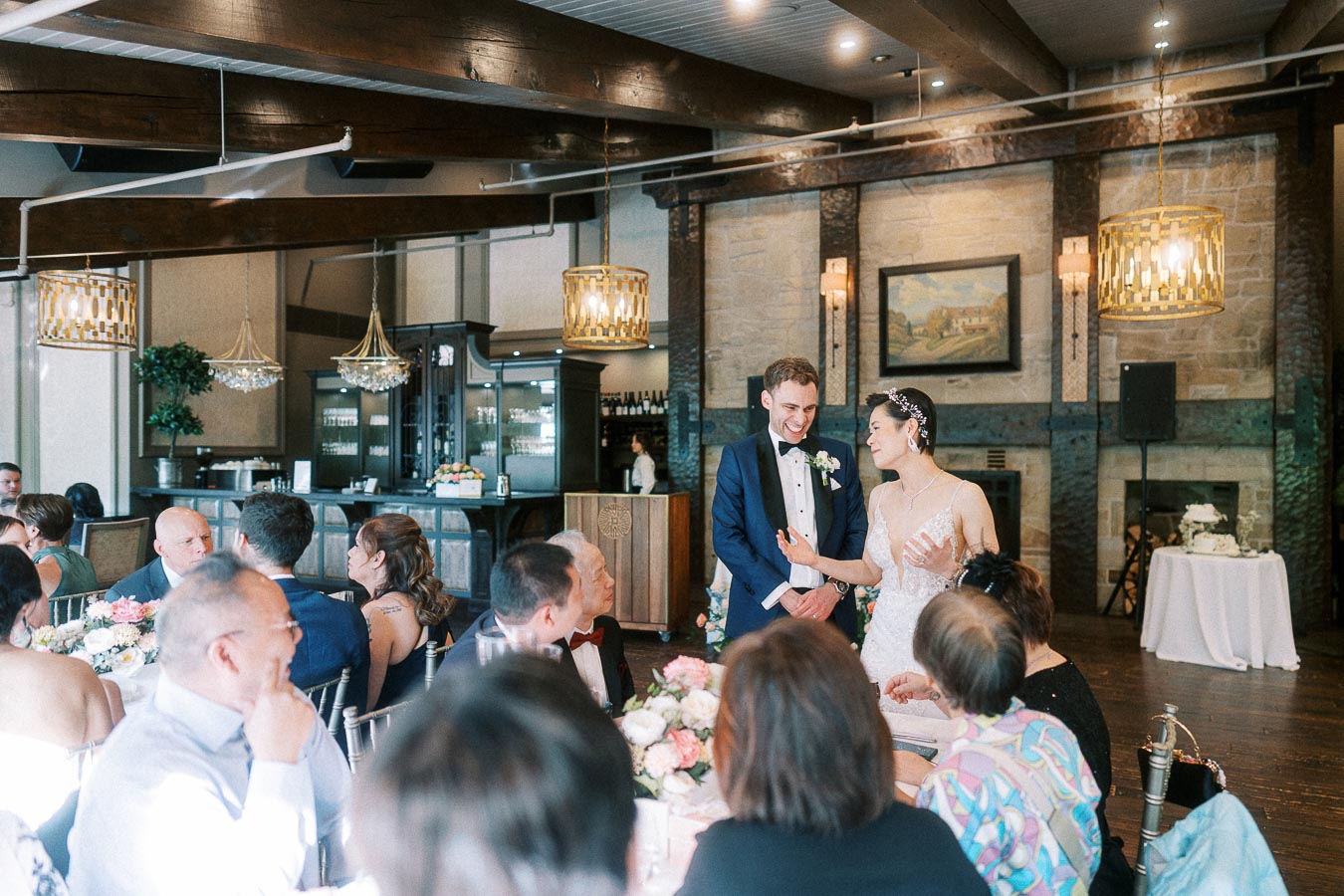 Bride and groom stand among seated guests during their Ancaster Mill wedding reception.