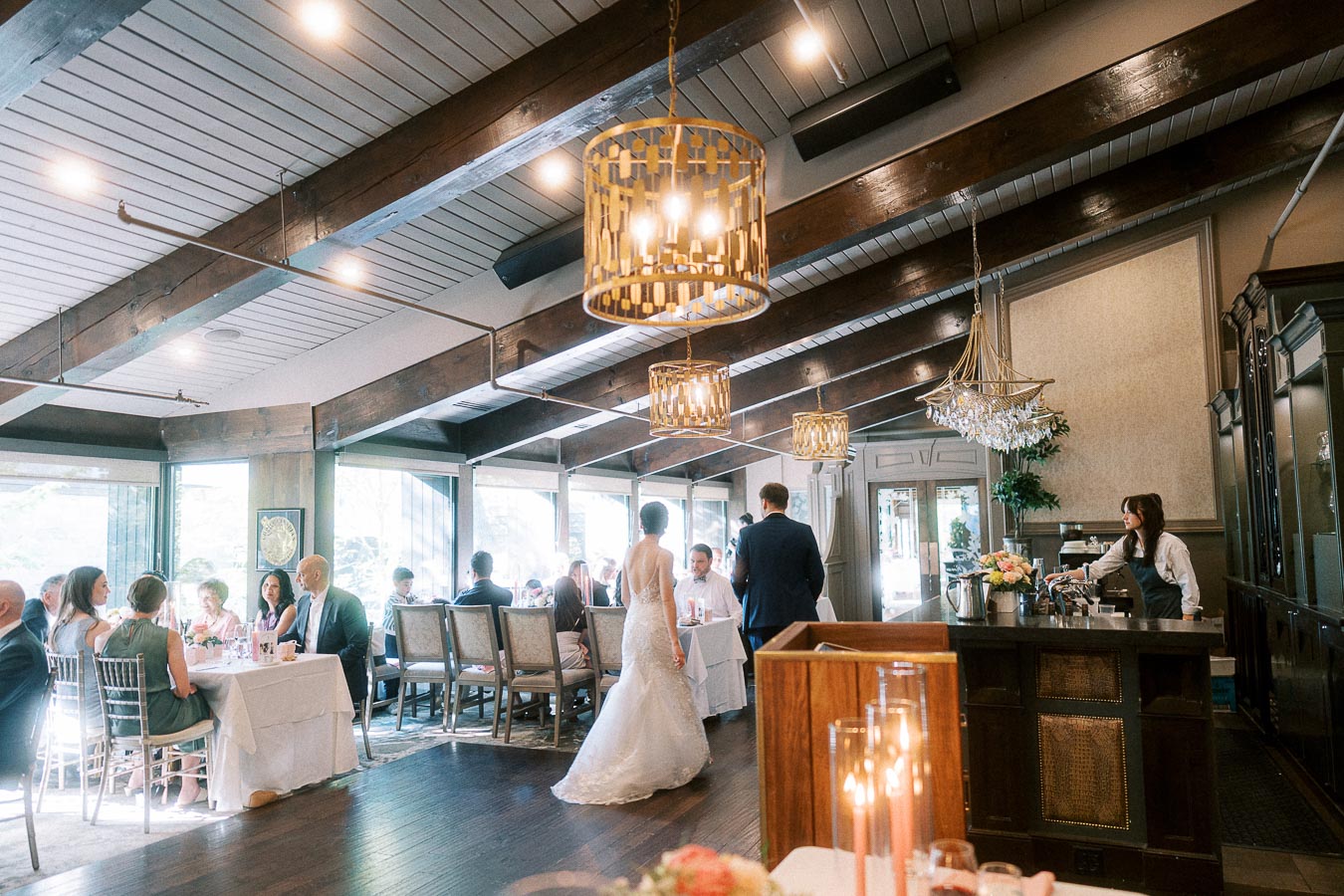 Bride and groom walk through an elegant reception room with seated wedding guests and chandeliers.