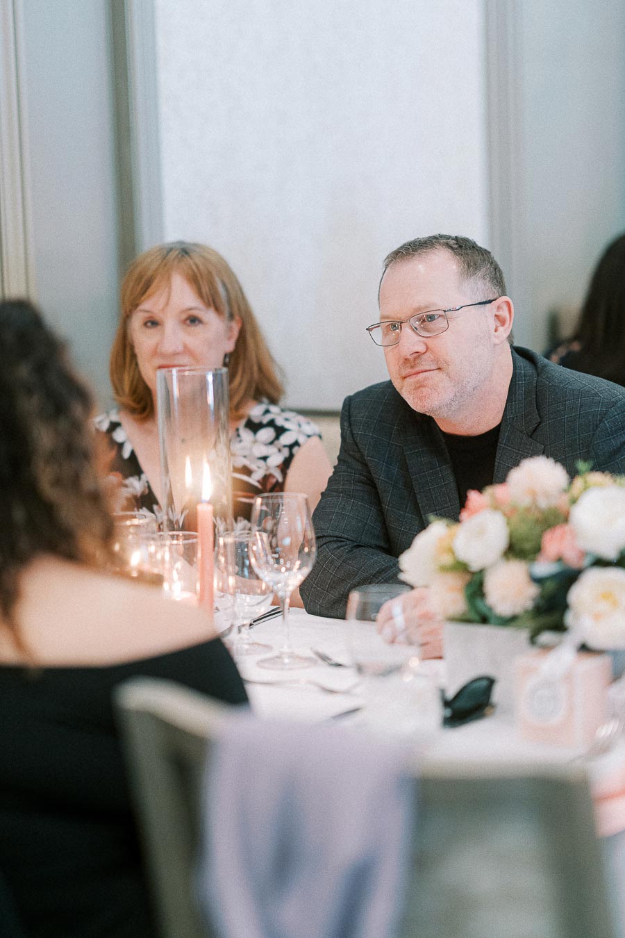 Guests seated at a candlelit reception table with floral centerpiece and wine glasses