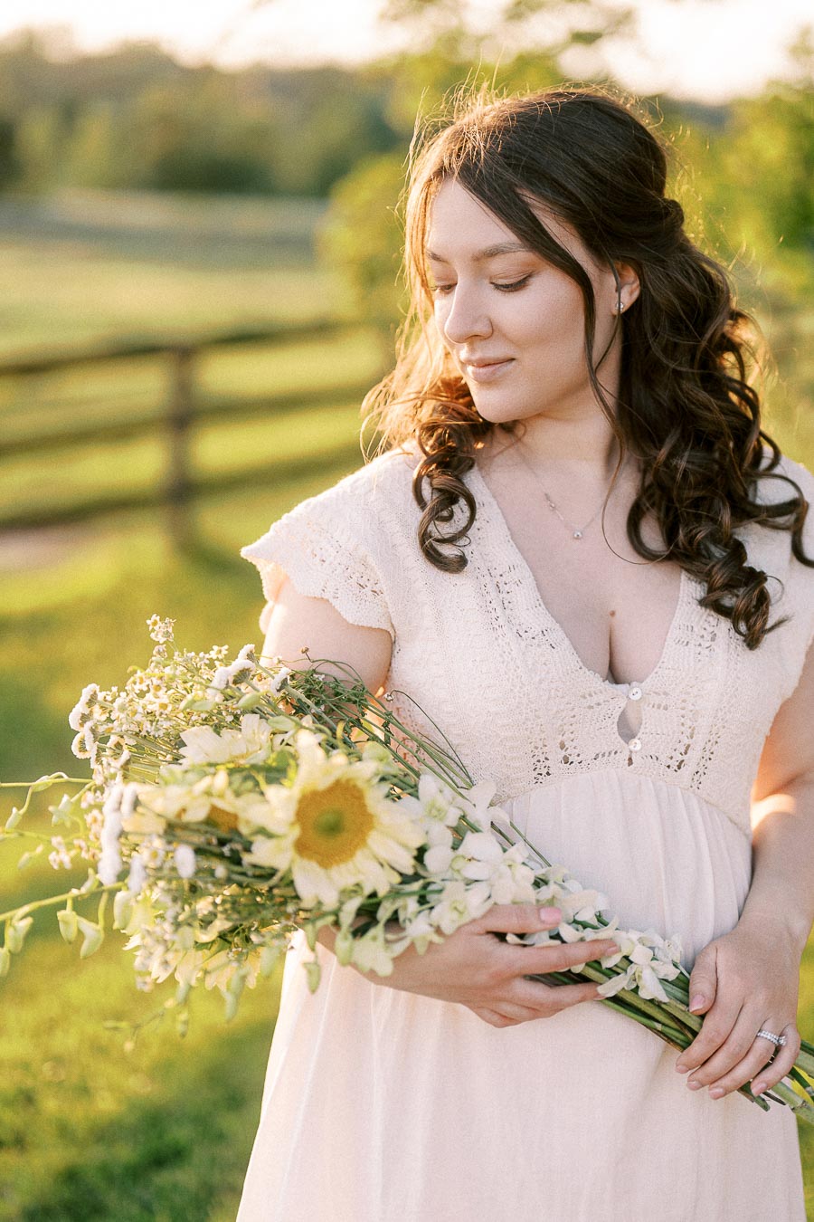Pregnant woman holding flowers in a sunlit field at The Green Acres
