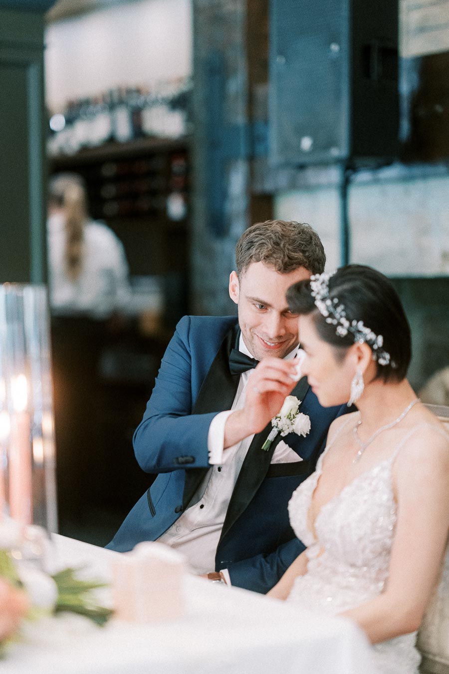 Groom gently touches the bride’s face as they sit together at a candlelit wedding reception table.