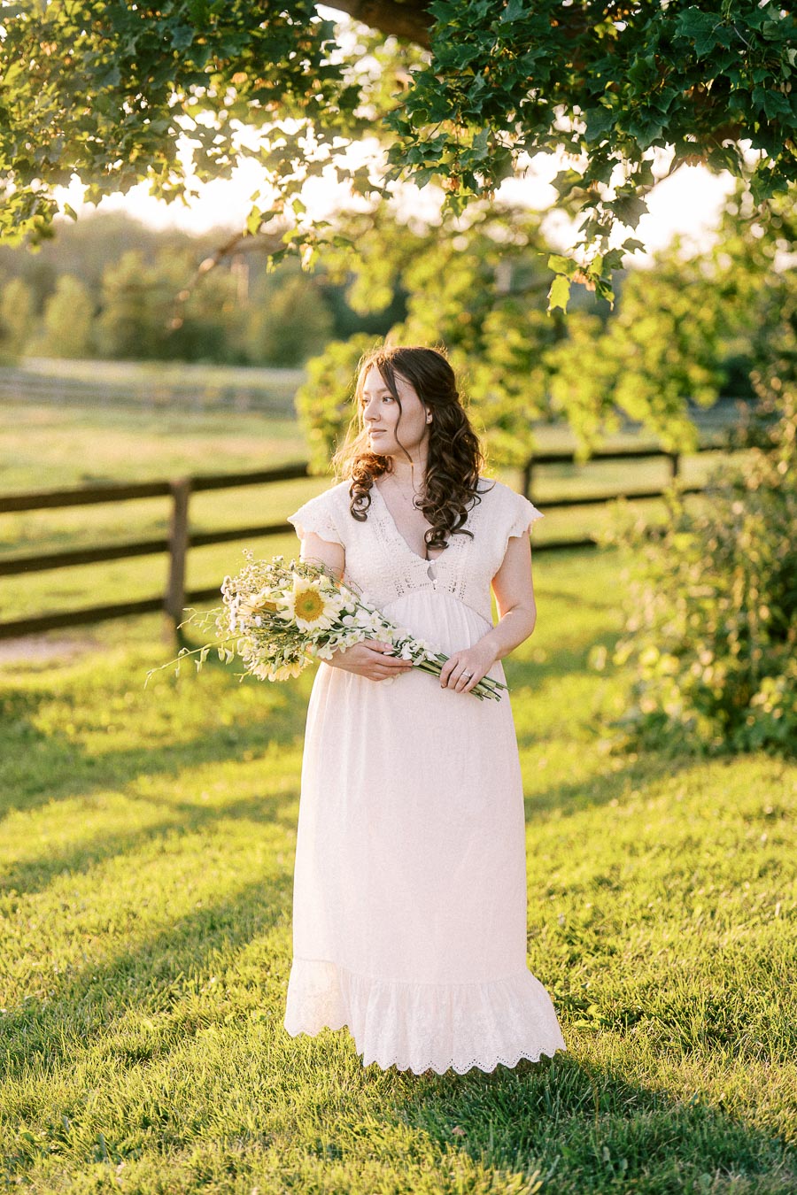 Pregnant woman in a pale dress holding flowers at The Green Acres