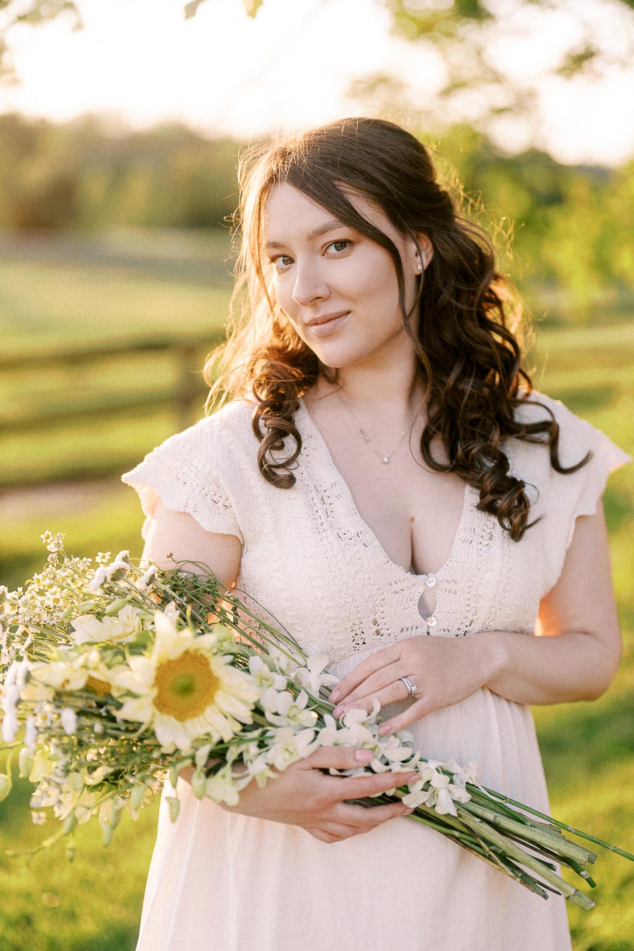 Expectant mother holding white flowers in a sunlit field at The Green Acres