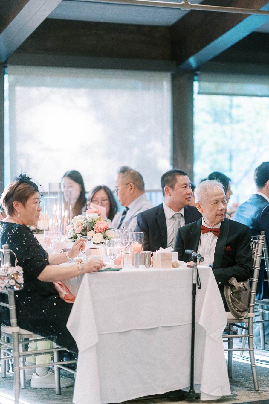 Wedding guests seated at a reception table with candles, florals, and soft window light at Ancaster Mill.