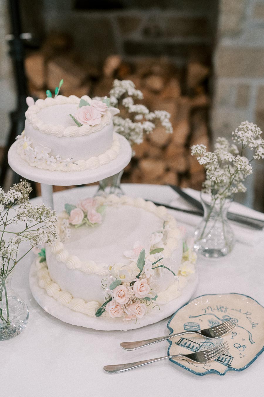 Two-tier white wedding cake with pink sugar flowers, baby's breath, forks, and a custom Miffy and Rawle cake plate.