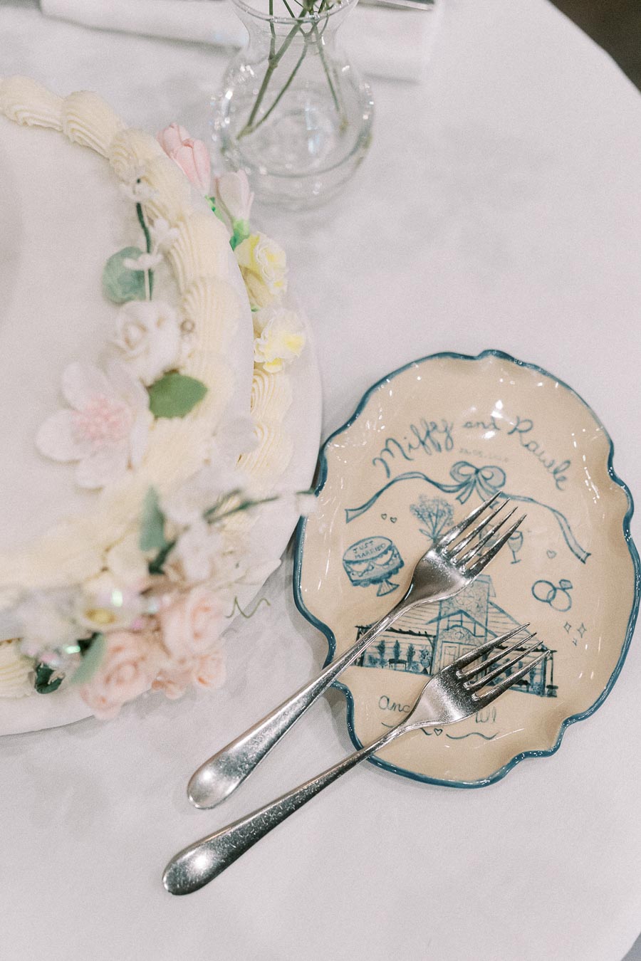 Wedding cake with floral icing beside a custom Miffy and Rawle plate and two forks