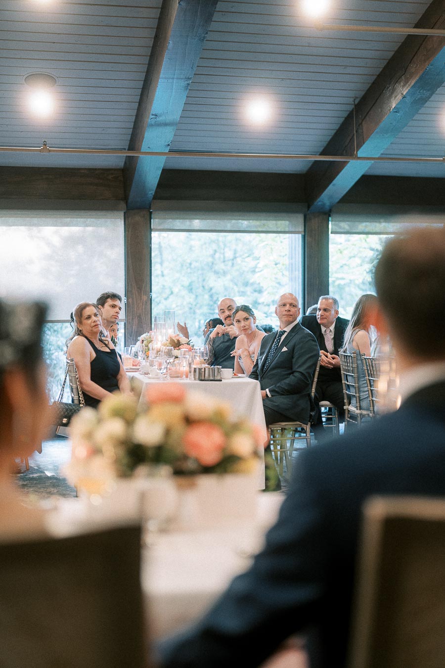 Wedding reception guests seated at long tables listen to a speaker inside Ancaster Mill.