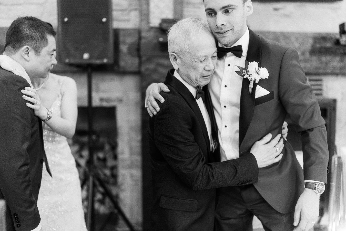 Rawle embraces an older man in a tuxedo during an emotional black-and-white wedding reception moment.