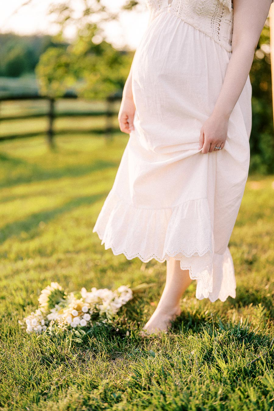 Pregnant woman in a white dress walking barefoot on grass at The Green Acres