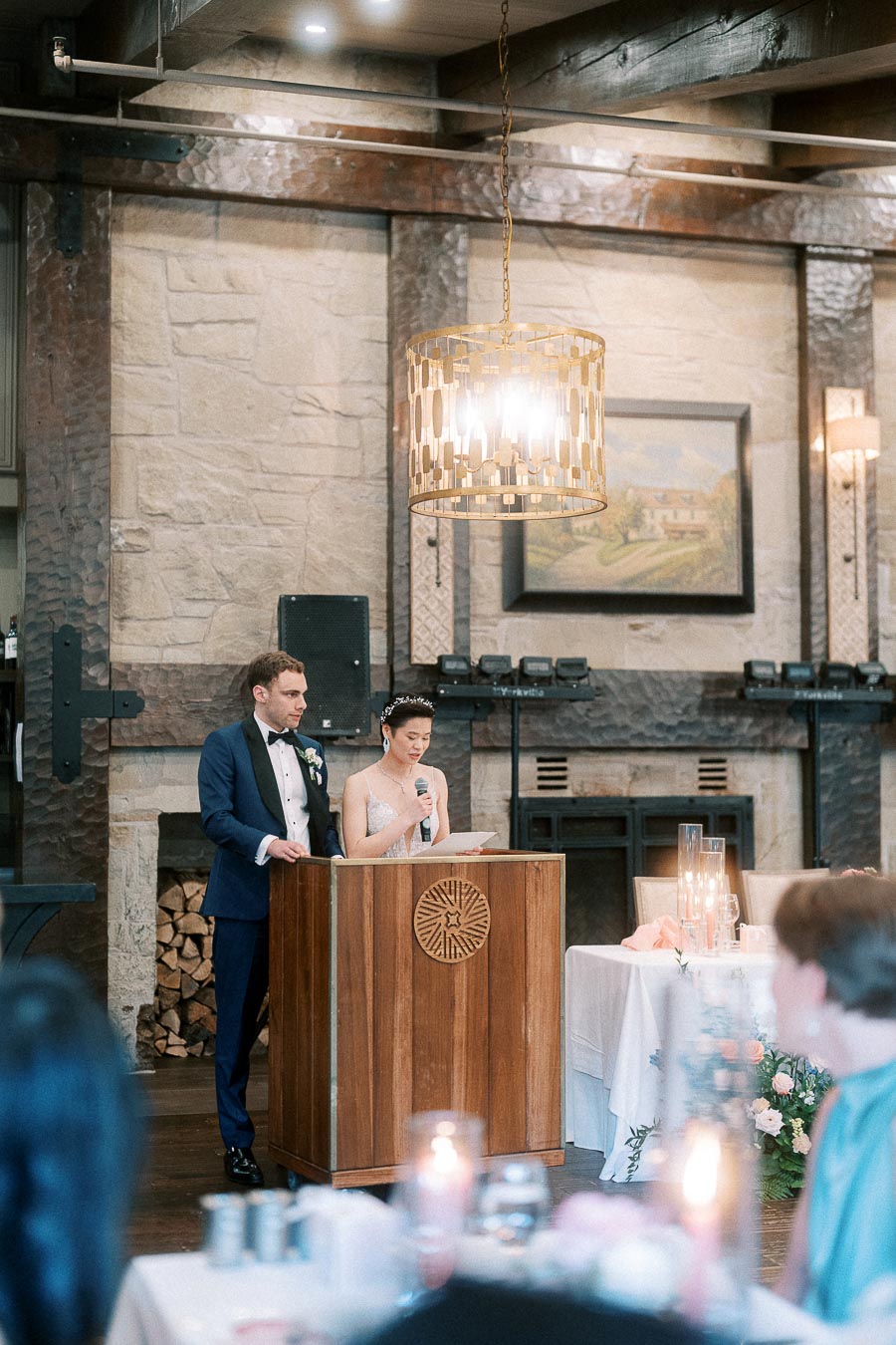 Miffy reads from a microphone beside Rawle at a wooden podium during their wedding reception speech.