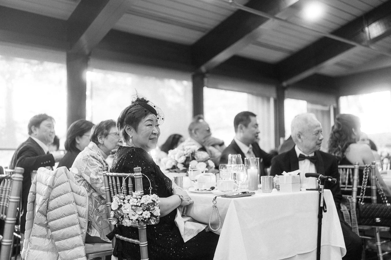 Black-and-white view of wedding guests seated at reception tables with candles, flowers and chiavari chairs.