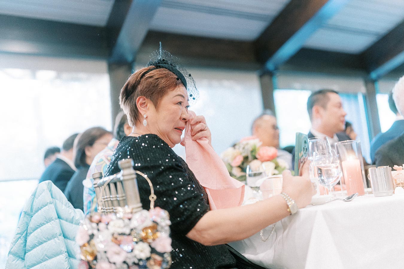Woman in a black sequined outfit wipes her eye while seated at a wedding reception table.