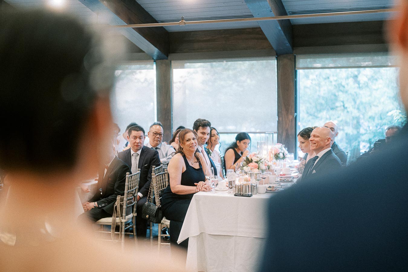 Wedding guests seated at a decorated reception table inside Ancaster Mill, framed by blurred foreground figures.