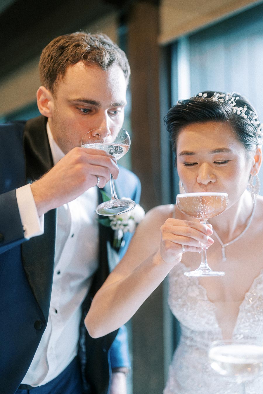 Bride and groom drinking champagne together at their wedding, wearing elegant bridal attire.