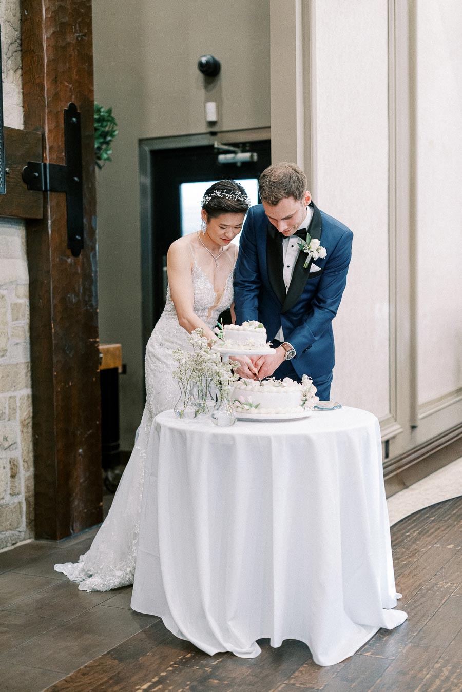 Elegant bride and groom in formal attire cutting a tiered wedding cake together at a reception, symbolizing their new beginning. Romantic and intimate setting with floral decorations.