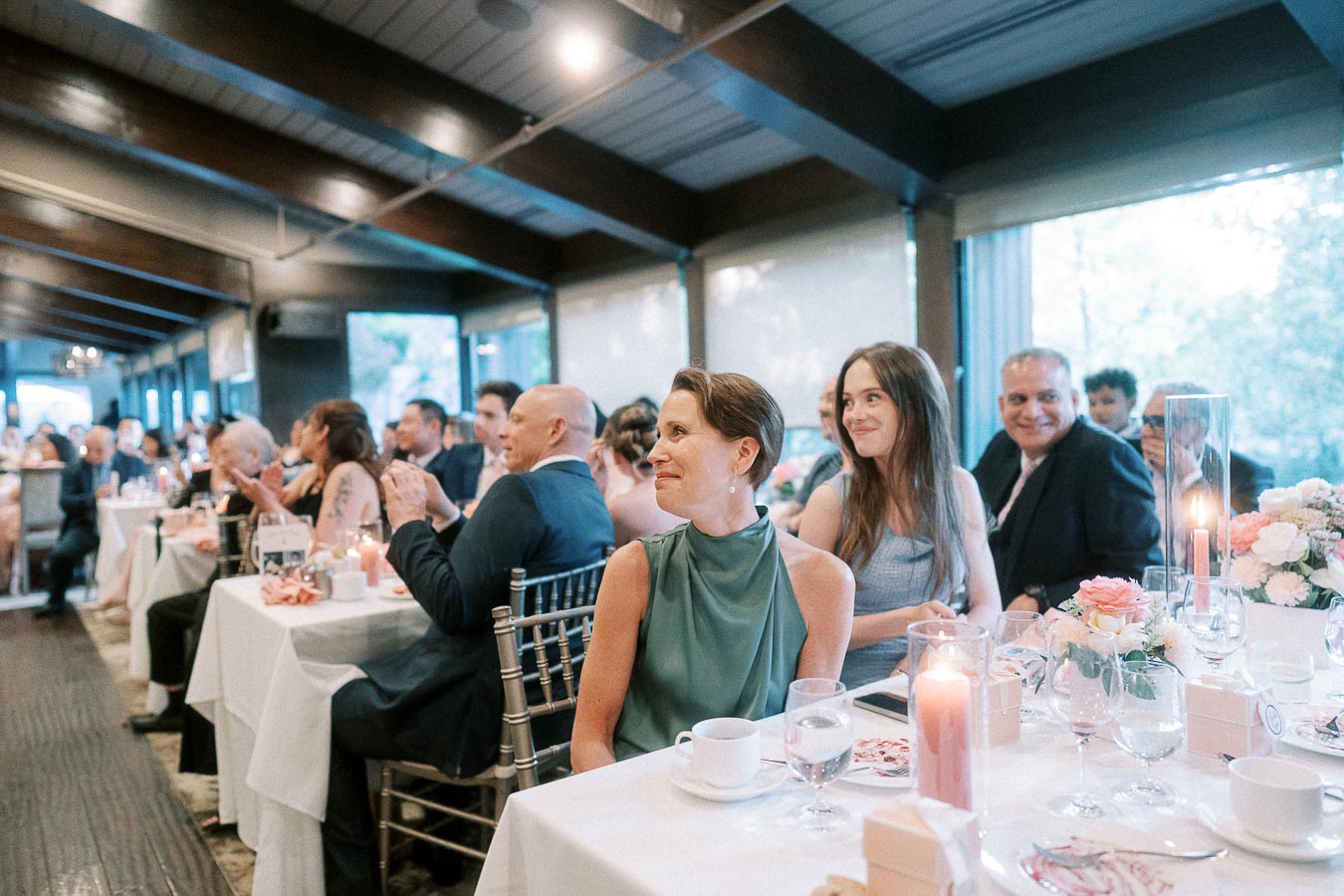 Guests seated at elegantly decorated tables, enjoying a celebration event in a beautifully lit indoor venue, with floral centerpieces and ambient candlelight creating a warm atmosphere.