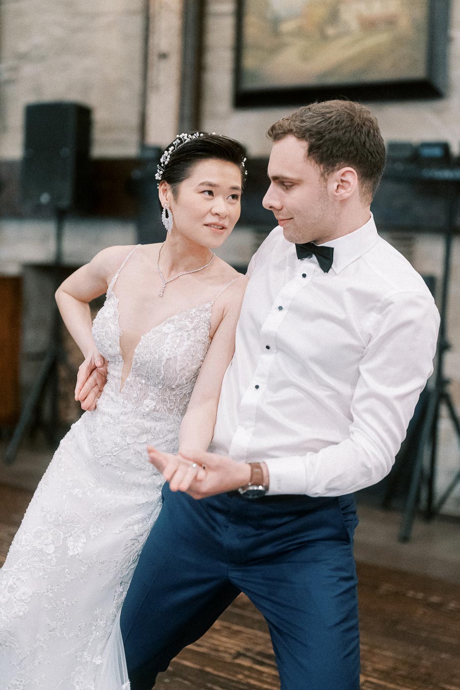 A joyful couple dancing at their wedding reception, the bride in an elegant lace gown and the groom in a classic white shirt and bow tie, showcasing a romantic moment on the dance floor.