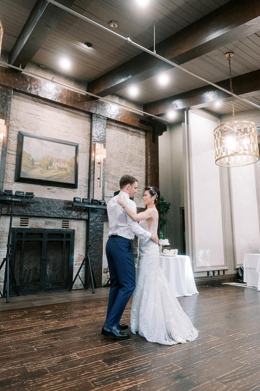 A couple enjoying a romantic first dance at their wedding reception in an elegant venue with wooden floors and subtle lighting.