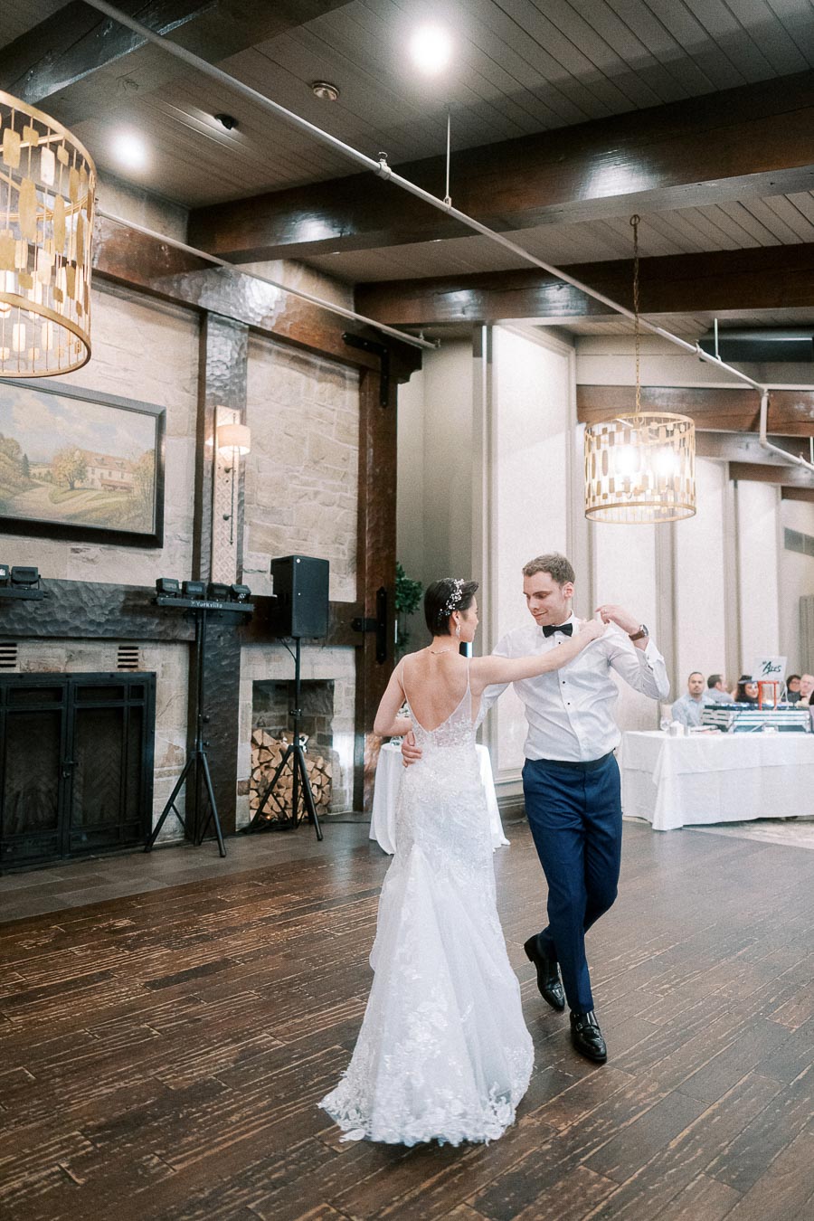 Elegant couple shares a romantic dance at a wedding reception in a rustic venue with wooden floors and ambient lighting.