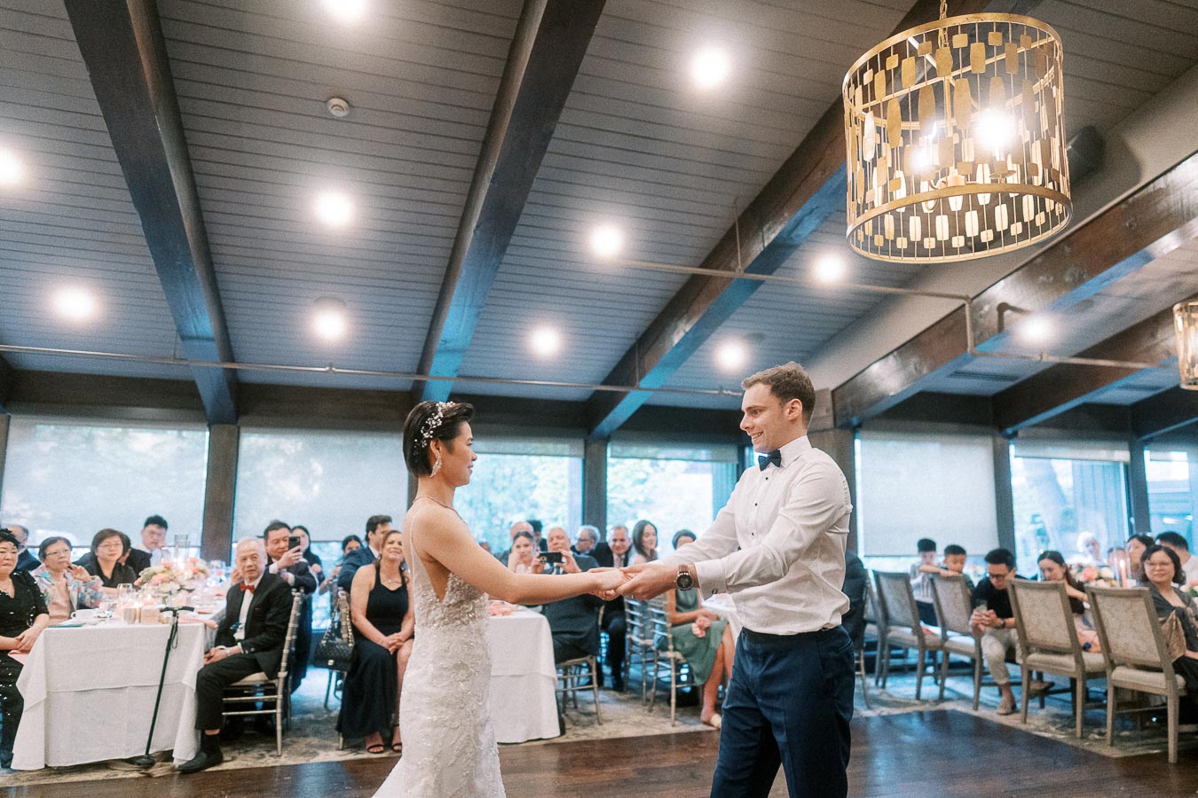 A couple shares a romantic first dance at their wedding reception in a beautifully decorated venue with guests seated around elegantly set tables.