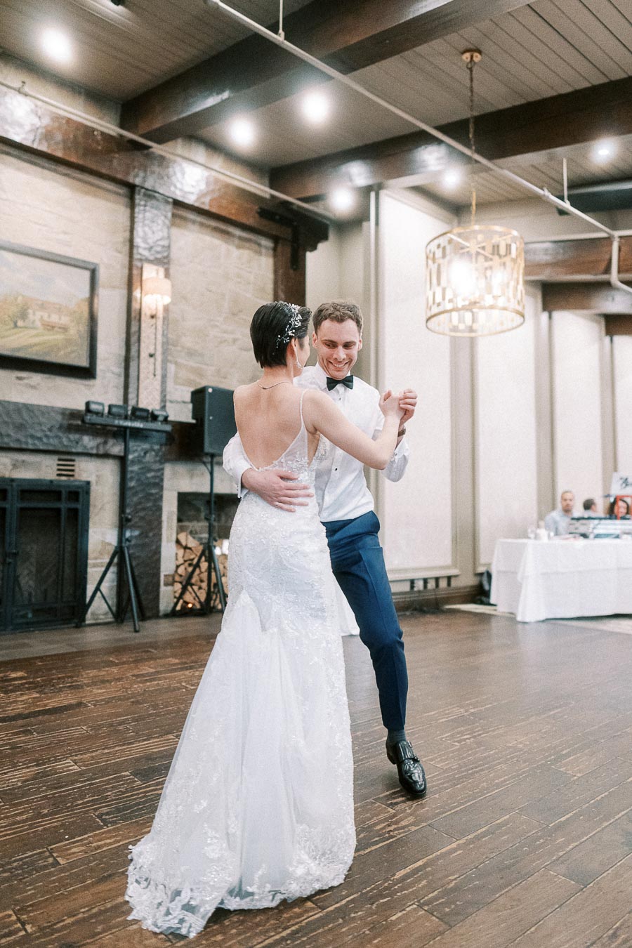 Bride and groom dancing at a wedding reception in an elegant, rustic venue with wooden floors and ambient lighting.
