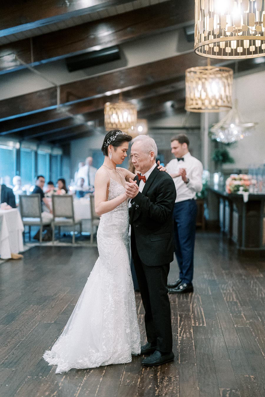 Bride and elderly man sharing a dance at wedding reception in elegantly decorated venue.