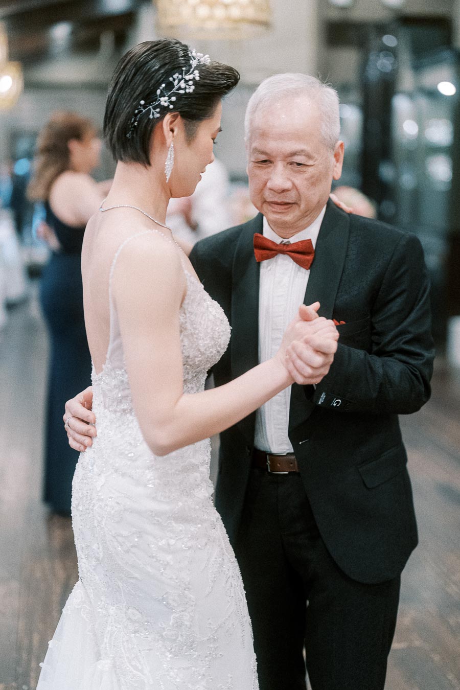 Elderly man in formal suit and young woman in wedding dress dancing at a wedding reception.
