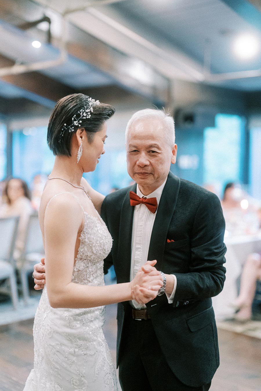 Elderly gentleman and bride dancing at a wedding reception, bride wearing a lace wedding dress and hair adorned with a decorative clip.