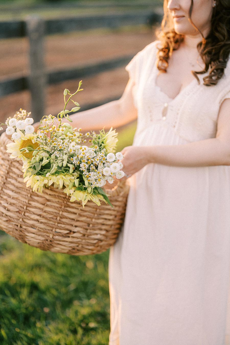 Pregnant woman in a pale dress holding a flower-filled basket at The Green Acres