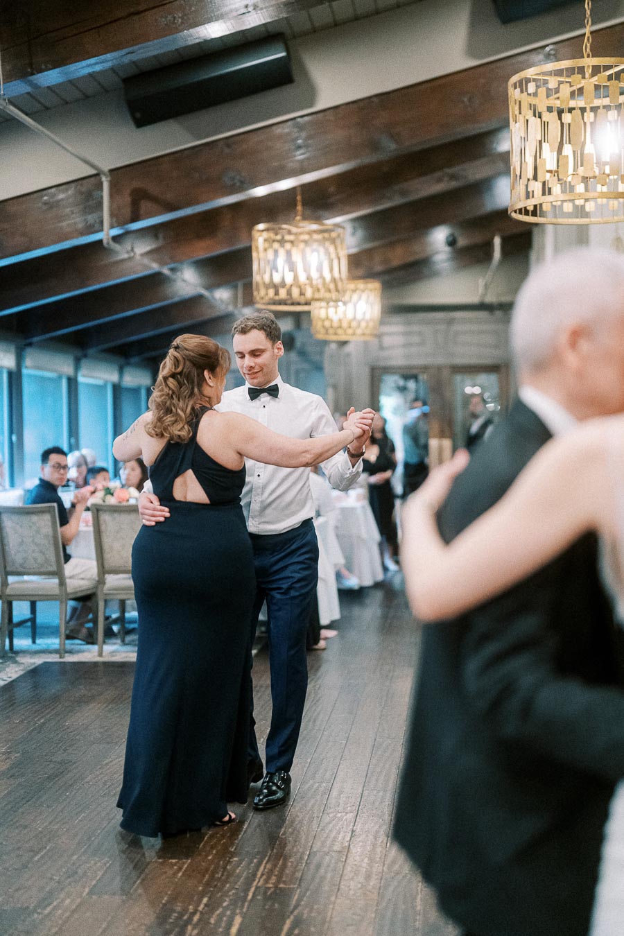 Elegant ballroom dance scene at a formal event, featuring a couple gracefully dancing in formal attire, surrounded by warmly lit chandeliers and seated guests.