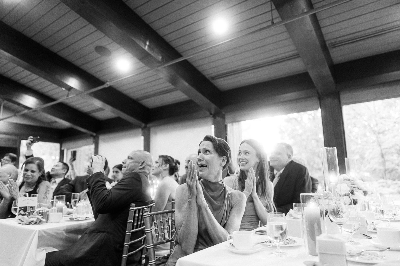 A joyful wedding reception with elegantly dressed guests clapping and smiling in a beautifully decorated banquet hall.
