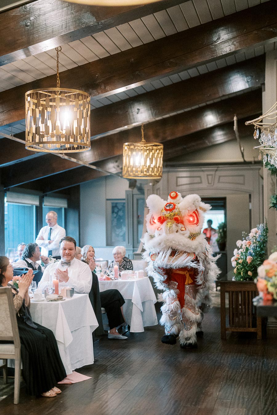 Lion dance performance at an indoor event with guests applauding, featuring elaborate decor and hanging lights.
