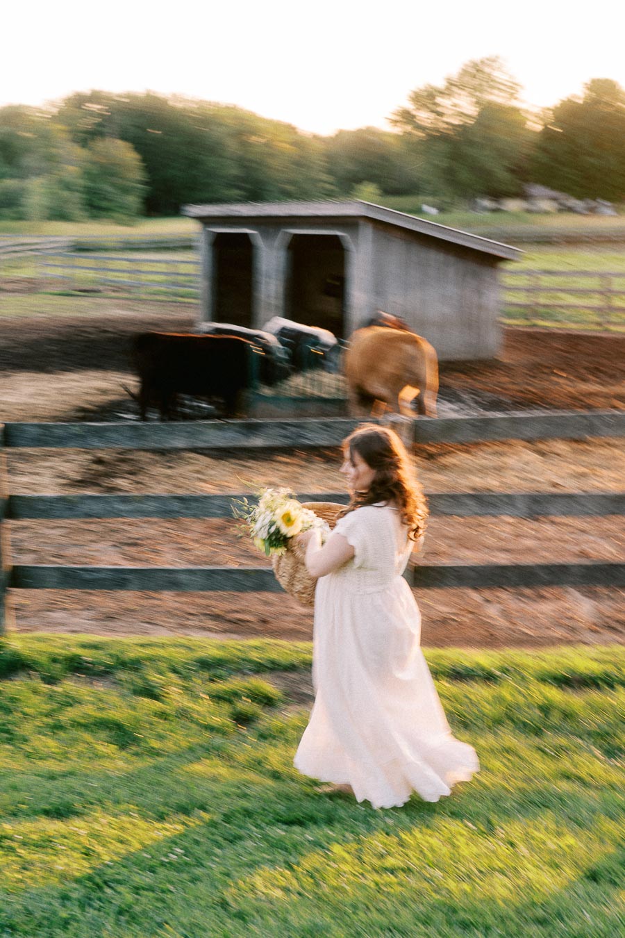 Pregnant woman in white dress walking by horse paddock at The Green Acres