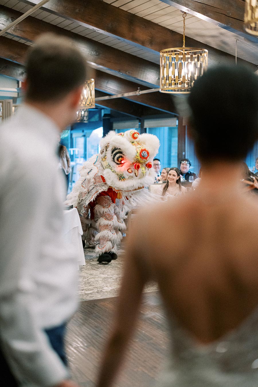 A vibrant lion dance performance at a wedding reception, with the bride and groom in the foreground, captivating guests in a beautifully decorated venue with wooden accents.
