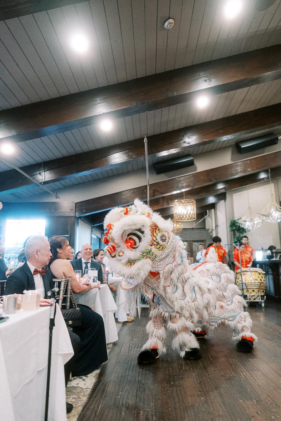 Lion dance performance at a formal indoor event with guests seated at decorated tables, showcasing traditional cultural celebration.