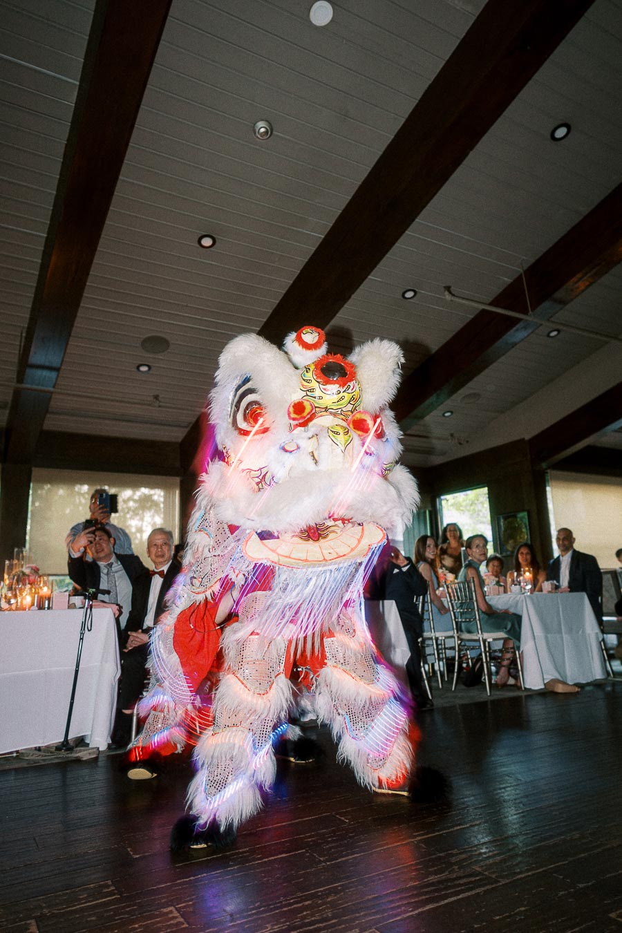 Lion dance performance at an indoor event with audience watching, featuring a colorful and illuminated costume.