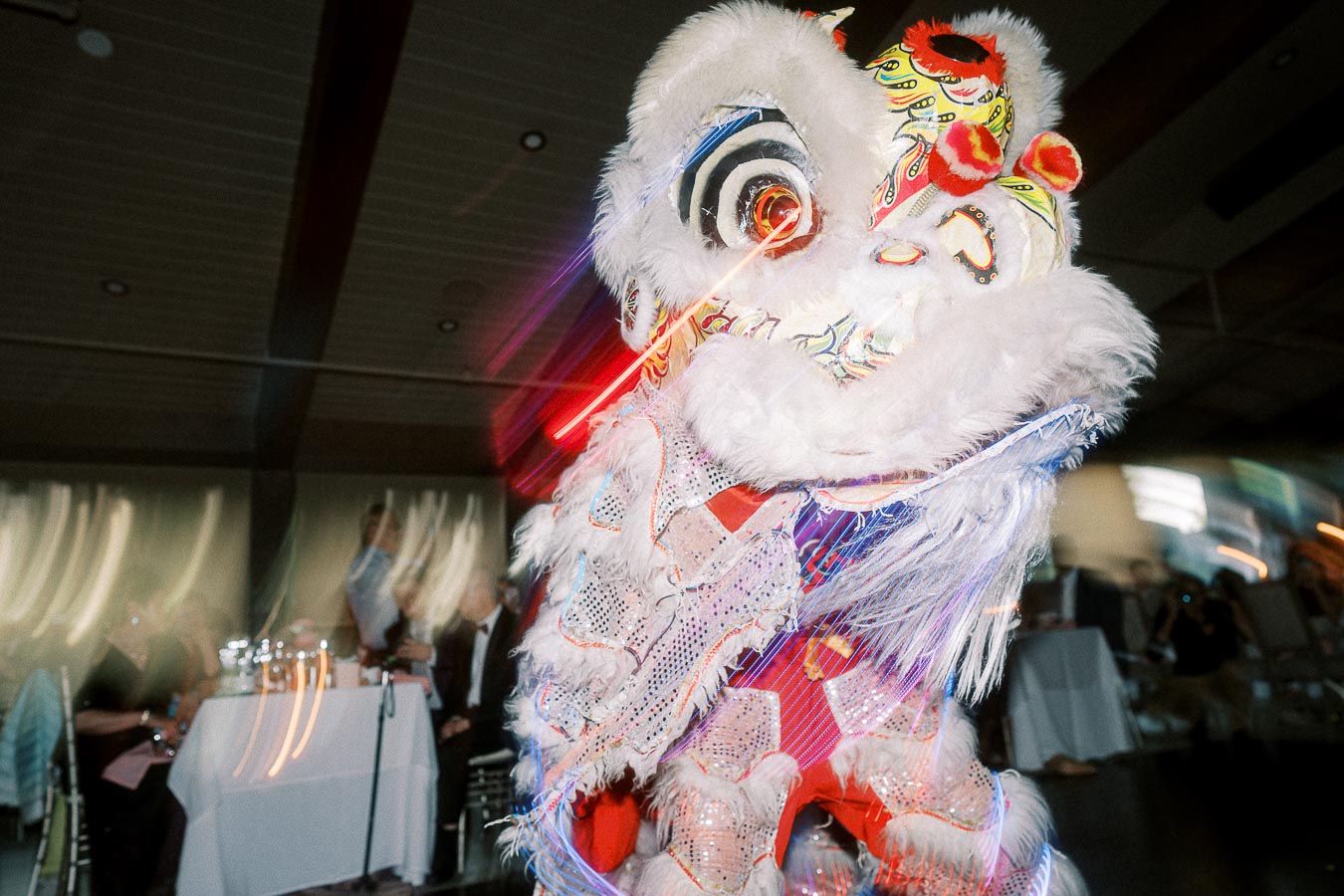 Lion dance performance at an indoor celebration, featuring a vibrant, colorful costume with intricate details and bright white fur.