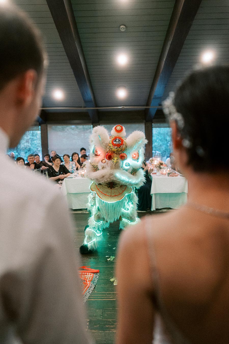 A glowing Chinese lion dance performance at a wedding reception, with guests in the background and the couple watching in the foreground.