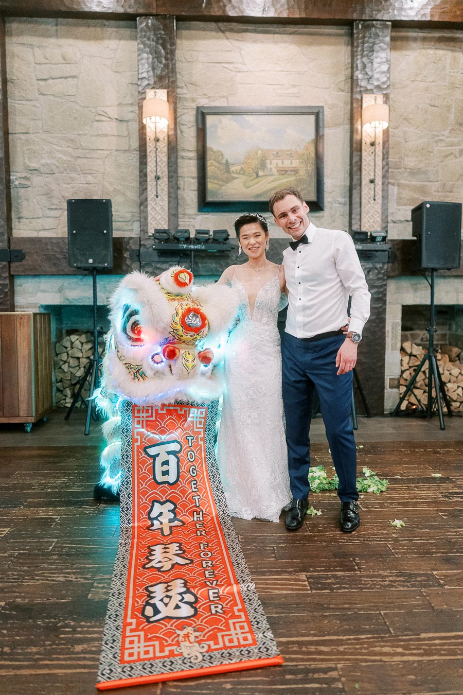 Wedding couple posing with a traditional Chinese dragon costume and banner inside a rustic venue, symbolizing cultural fusion and celebration.