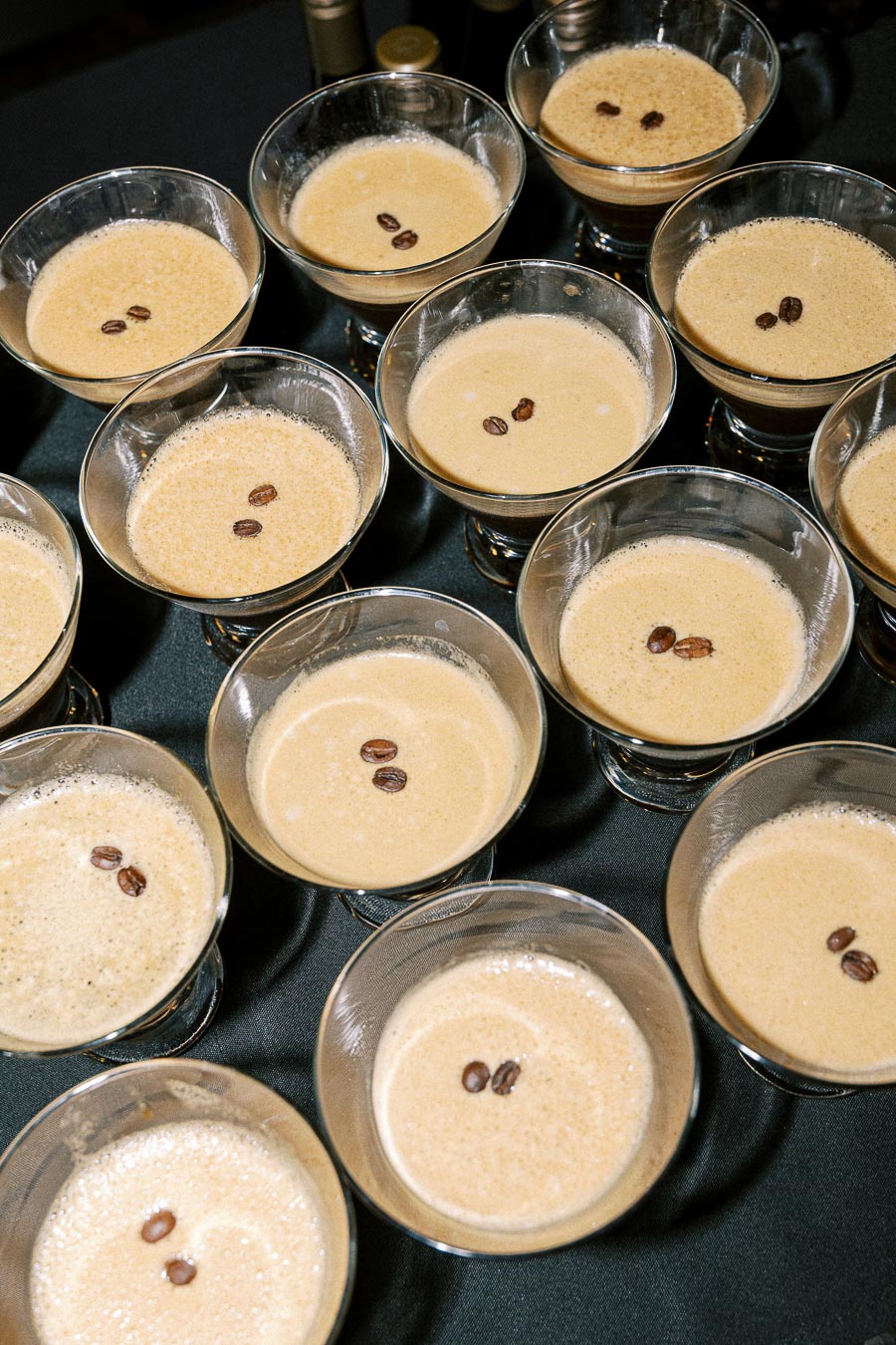 Overhead view of multiple espresso martinis garnished with coffee beans, arranged on a dark table.