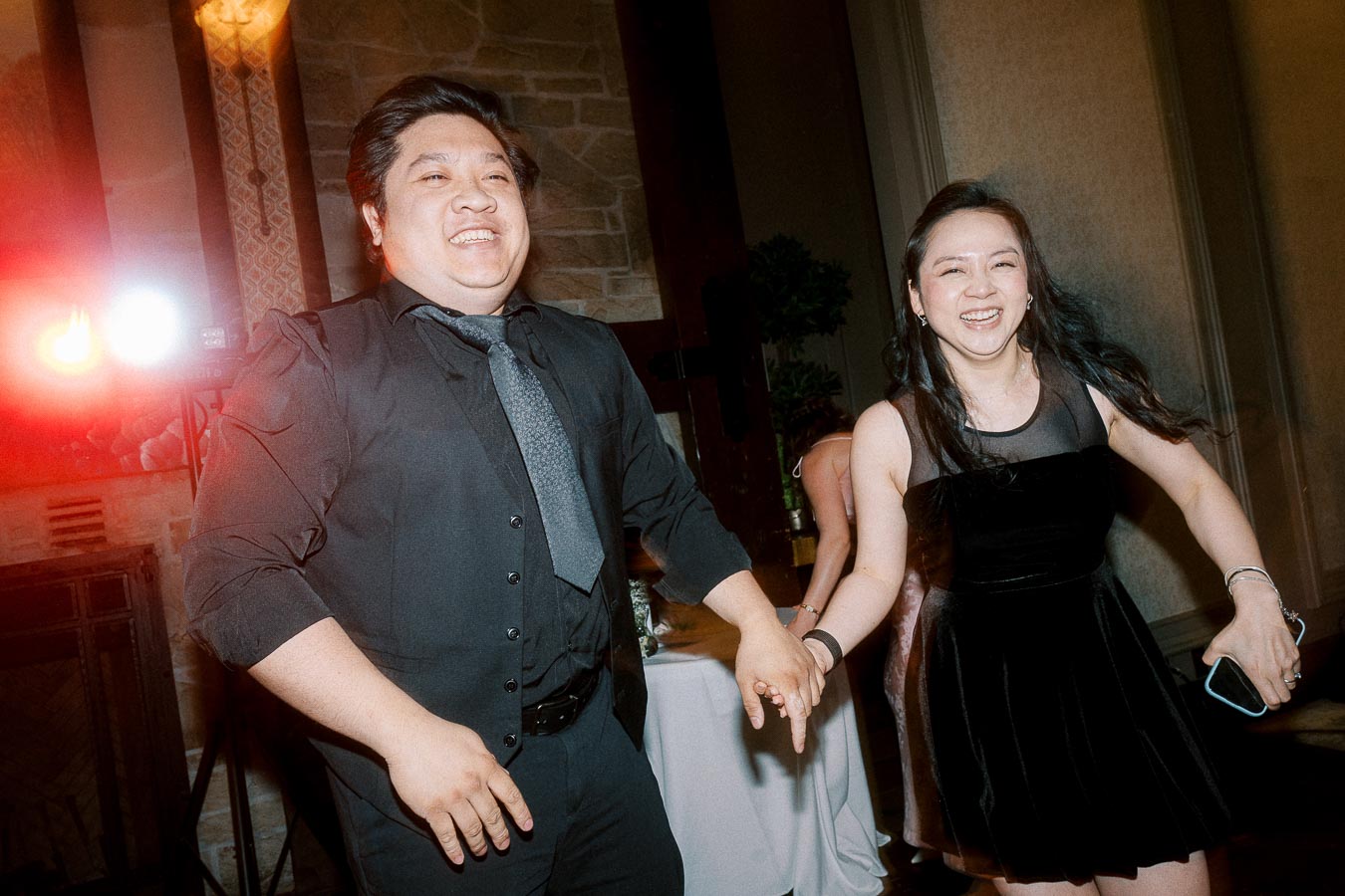 Two people joyfully dancing together at an indoor event, with warm lighting and a stone wall backdrop adding to the festive atmosphere.