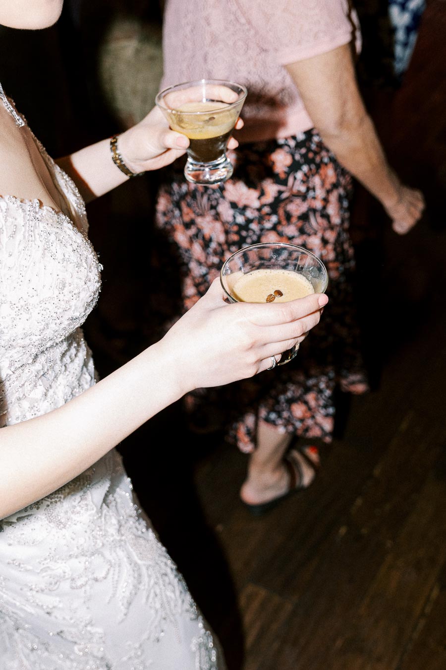 Bride holding espresso martini cocktails during wedding reception, wearing an elegant white gown with intricate beadwork.
