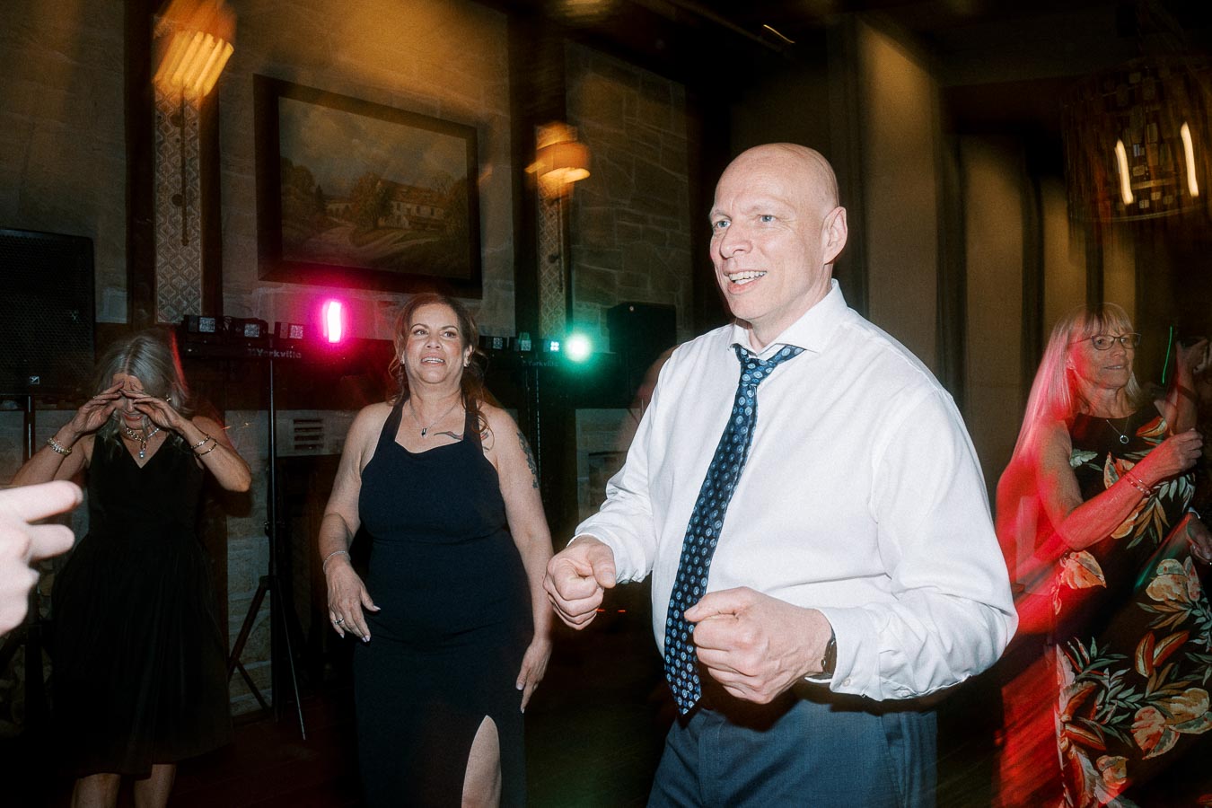 A group of people enjoying a lively dance at an indoor party, featuring vibrant lighting and a cheerful atmosphere.