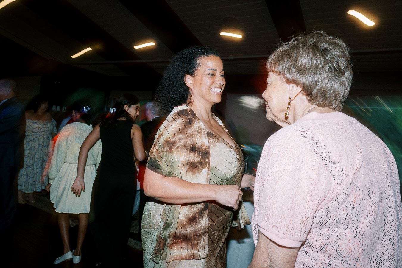 Women dancing and smiling at a lively indoor party, with colorful lighting and a joyful atmosphere.