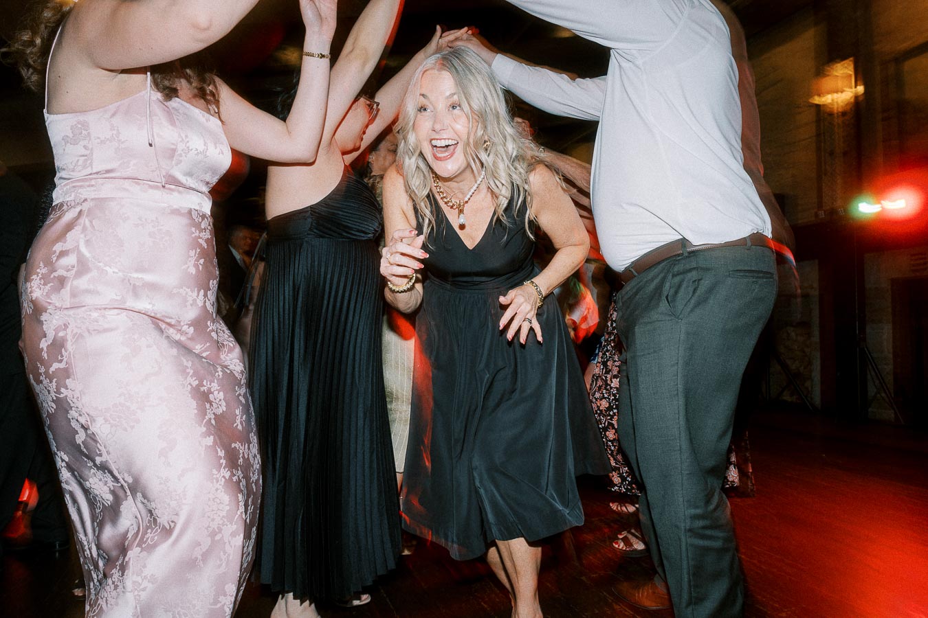A joyful group of people dancing energetically at a lively indoor event, capturing a festive atmosphere with vibrant lighting and smiling faces.